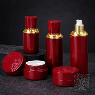 Glossy red skincare bottles and cosmetic jars with gold collars, arranged with one open jar on a dark stone surface.