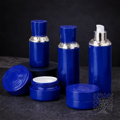 Deep blue skincare bottles and cosmetic jars with silver accents, displayed with open jar detail on textured backdrop.