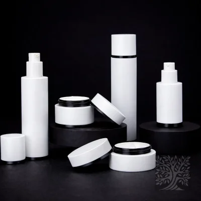 White skincare bottles and cosmetic jars with black accents, arranged on dark pedestals with open jar lids displayed.