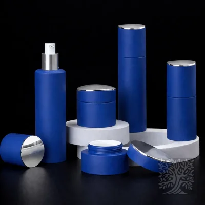 Matte cobalt blue bottles and jars with silver caps, displayed on tiered white platforms with lids set aside.