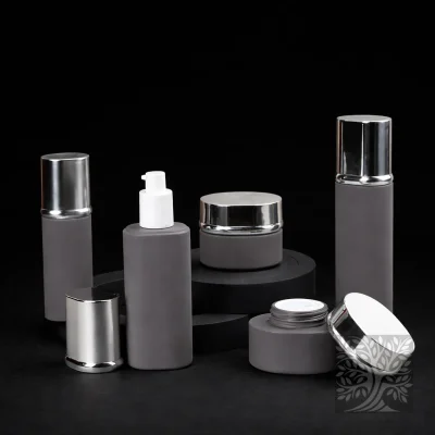 Soft gray cosmetic bottles and jars with chrome lids, arranged in a minimal composition on stepped black platforms.