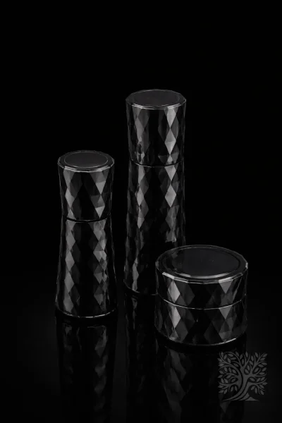 Smoked black faceted acrylic skincare bottles and cosmetic jar set with geometric texture, arranged on dark surface.
