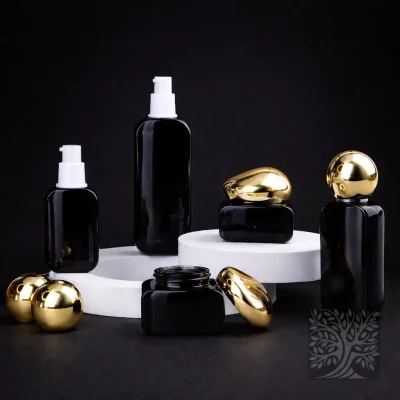 Gloss black glass skincare bottles and cosmetic jars with gold caps, including a pump bottle, arranged on a white display base.