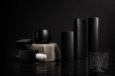 Gloss black skincare bottles and a rounded cosmetic jar, styled in a minimal arrangement on a textured stone platform.