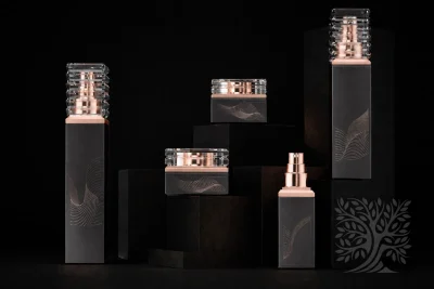 Charcoal gray skincare bottles and cosmetic jars with rose gold accents, displayed on elevated black platforms.