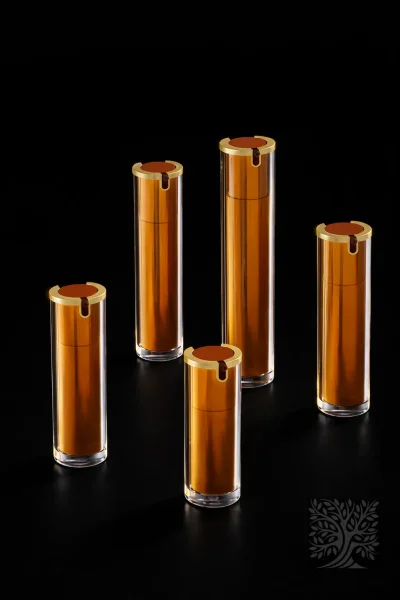 Warm amber acrylic bottles with gold-accented tops and clear outer shells, styled in a coordinated cosmetic packaging set.