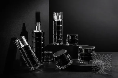 Clear acrylic skincare bottles and cosmetic jars with black accents, arranged on black platforms with open jar display.