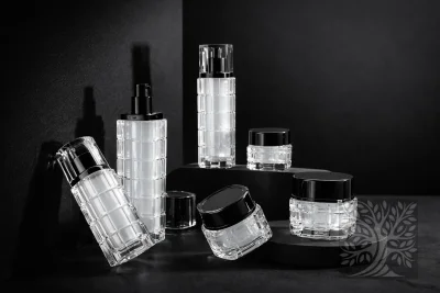 Clear acrylic skincare bottles and cosmetic jars with black caps, displayed on dark platforms with tilted jar arrangement.
