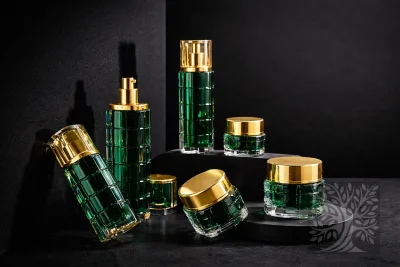 Emerald green acrylic skincare bottles and cosmetic jars with gold caps, arranged on black risers with open jar view.