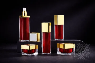 Red acrylic skincare bottles with gold caps and matching cosmetic jars, arranged on blocks with bold contrast display.