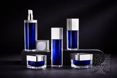 Deep cobalt blue acrylic skincare bottles with silver caps and cosmetic jars, arranged on layered stands with clean symmetry.