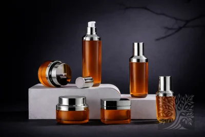 Amber-toned acrylic skincare bottles and cosmetic jars with silver caps, arranged on white stands with open jar detail.