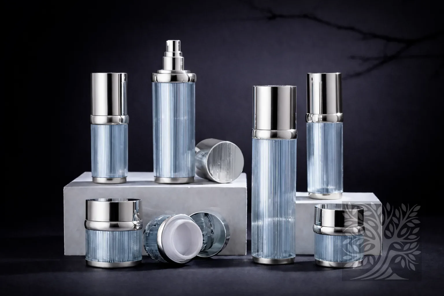 Frosted light blue ribbed acrylic skincare bottles and cosmetic jars with silver caps, arranged on white platforms.